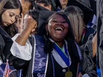 A close-up shot of a joyful female graduate laughing excitedly and raising her fist in celebration among her peers.