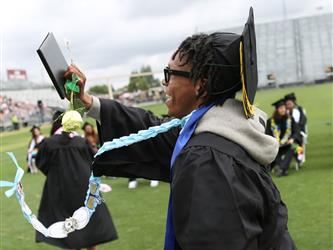 High school graduate smiling and waving to the crowd in the stands.