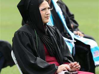 High school graduate sitting in chair at graduation cermony.
