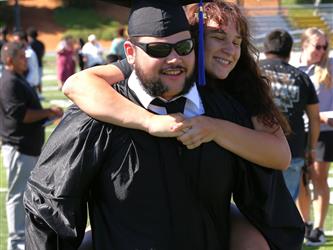 Adult Education graduate smiling brightly and giving a family member at piggy back ride at graduation ceremony.