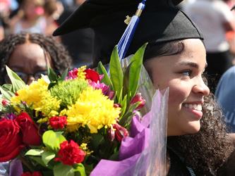 high school graduate smiling and holding a boquet of flowers.