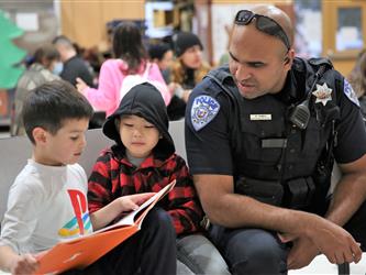police officer sitting with two students reading a book