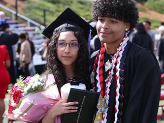 two high school graduates smiling and posing for a photo.