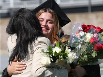 Adult Education graduate smiling brightly and hugging family member at graduation ceremony.