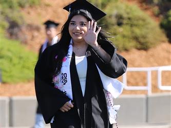 high school graduate walking, smiling and waving.