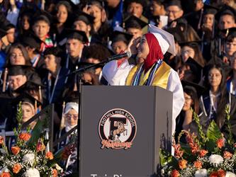 A female graduate in a red hijab and white gown speaks at a podium featuring the Foothill High School Mustangs logo.