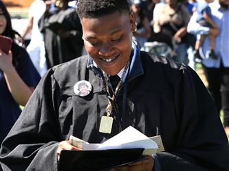 Adult Education graduate smiling warmly while looking down at his diploma at graduation ceremony.