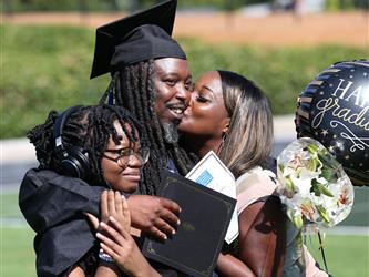 Adult Education graduate smiling brightly and hugging family members at graduation ceremony.