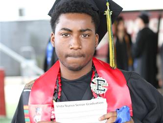 High school graduate smiling holding up a piece of paper.