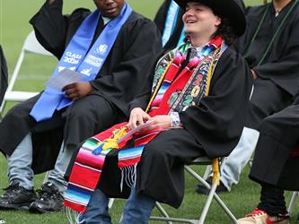 High school graduate smiling while sitting in chair. Wearing a cowboy hat and boots.