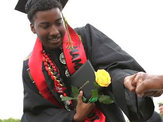 High school graduate smiling and fist-bumping an adult.