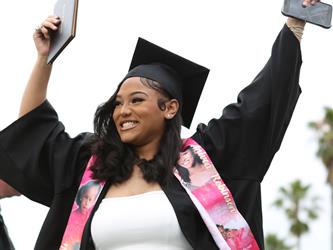 High school graduate smiling while raising arms in the air celebrating.