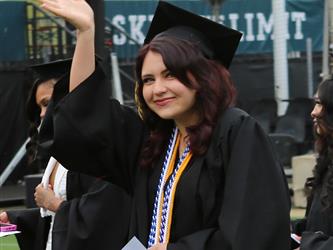 High school graduate smiling and waving.