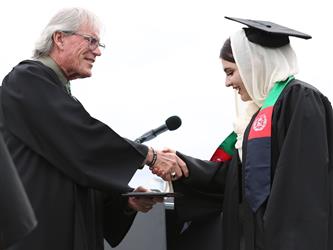 High school graduate smiling and shaking hands with the principal.