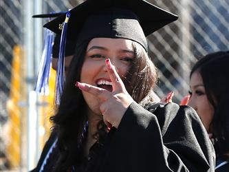 high school graduate holding up a peace sign with fingers and smiling.