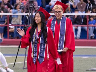 two high school graduates walking together and smiling