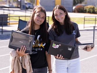 two high school girls smiling and holding laptops in their arms