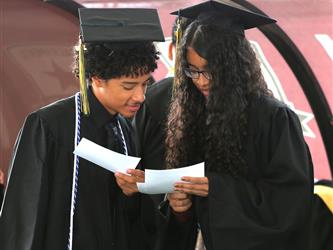 Two High school graduates reading a piece of paper.