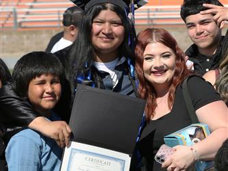 Adult Education graduate smiling brightly while hugging family members at graduation ceremony.