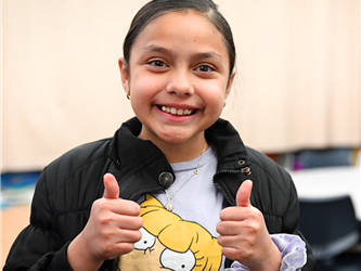 elementary student with two thumbs up smiling