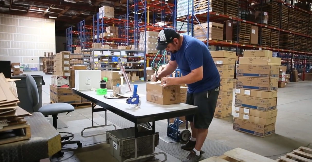 A man labeling a box in a warehouse full of boxes.