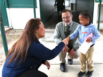 Superintendent Dr. Carroz shaking hands with young student with principal smiling in the background.