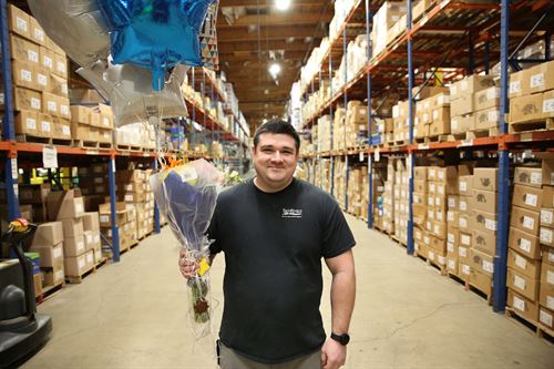 Man standing in warehouse holding a balloon bouquet. 